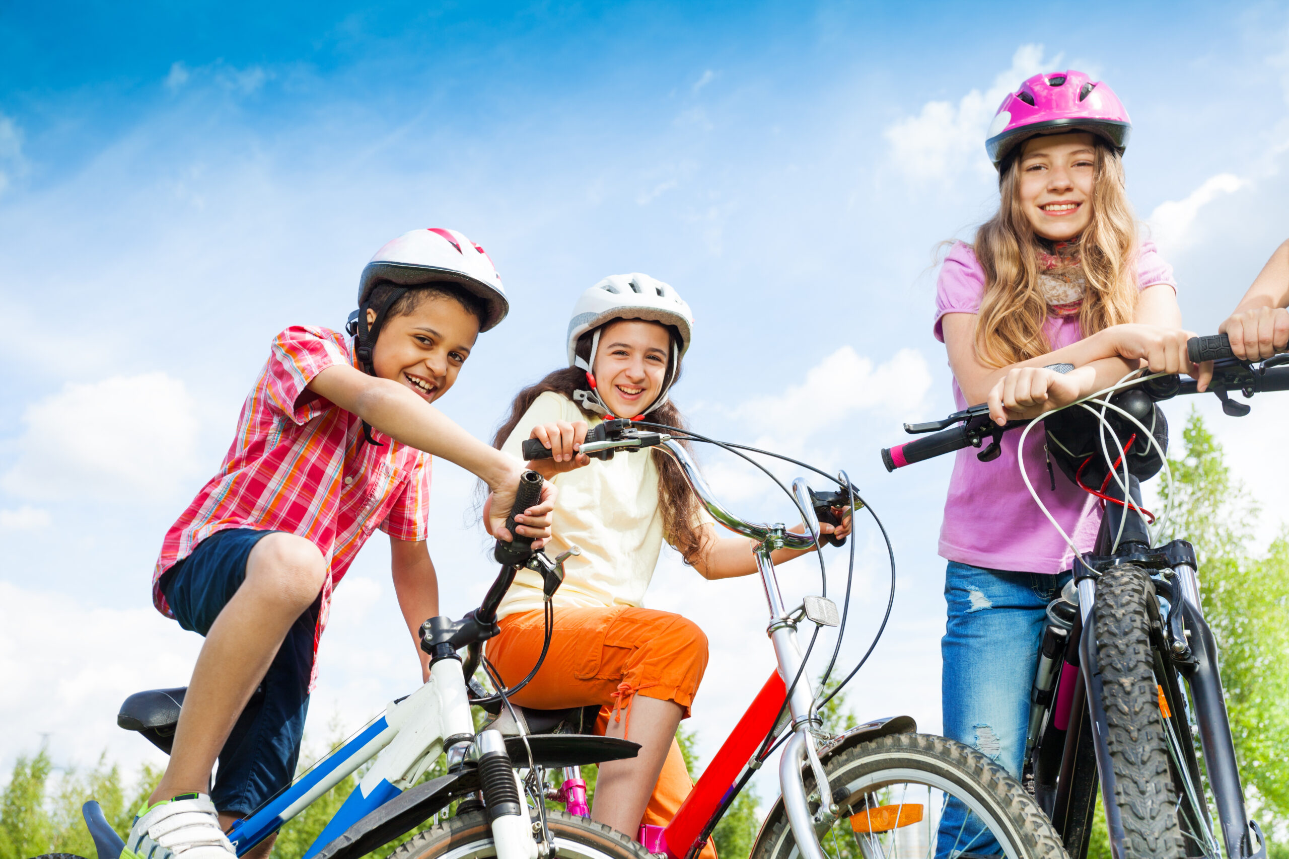 Three laughing kids in helmets hold bike handle-bars and are ready to ride a bike