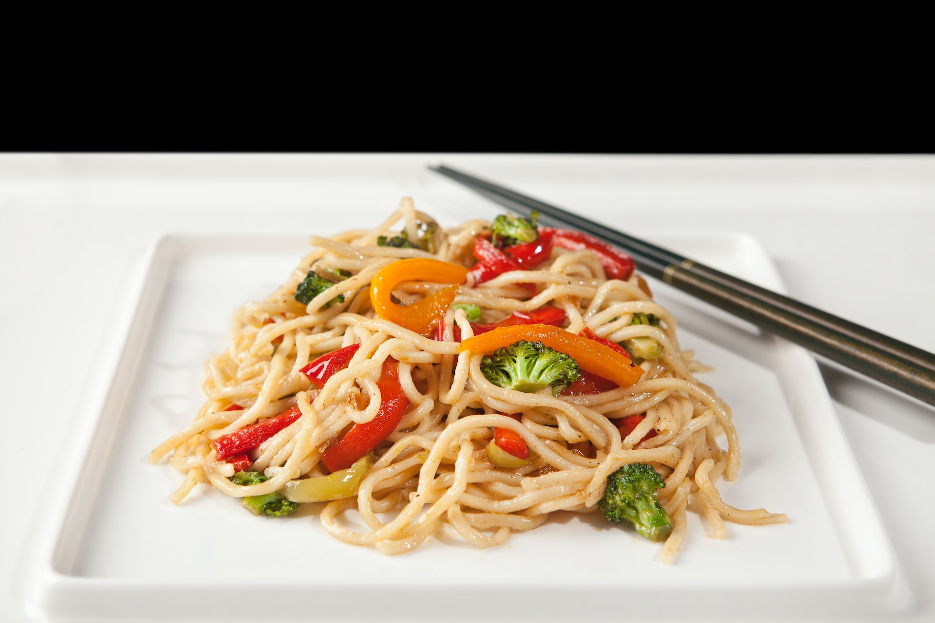 A plate of a noodle and vegetable stir fry with chopsticks is pictured.