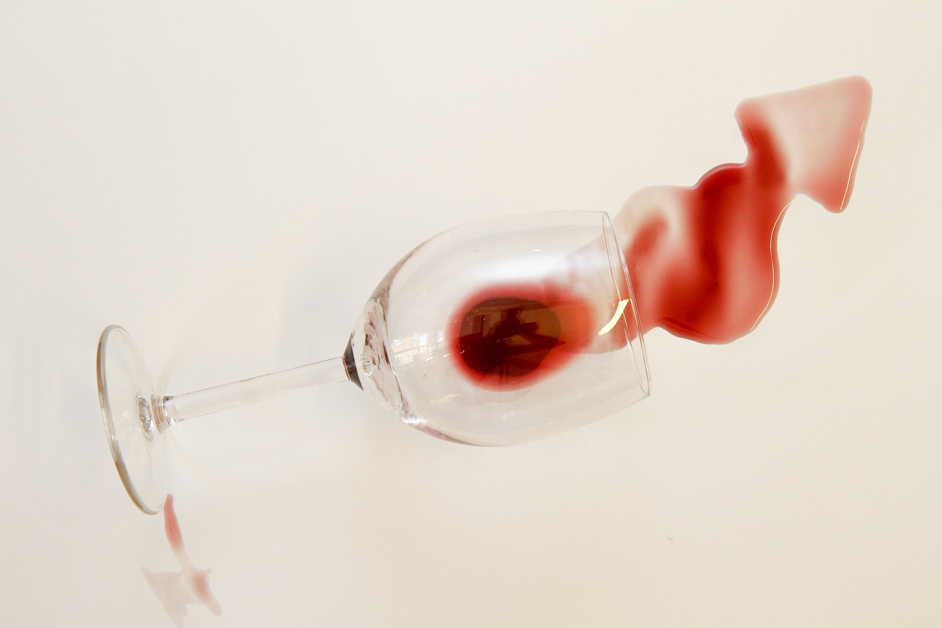 A glass of red wine is on its side, spilling the wine out on a white table top.