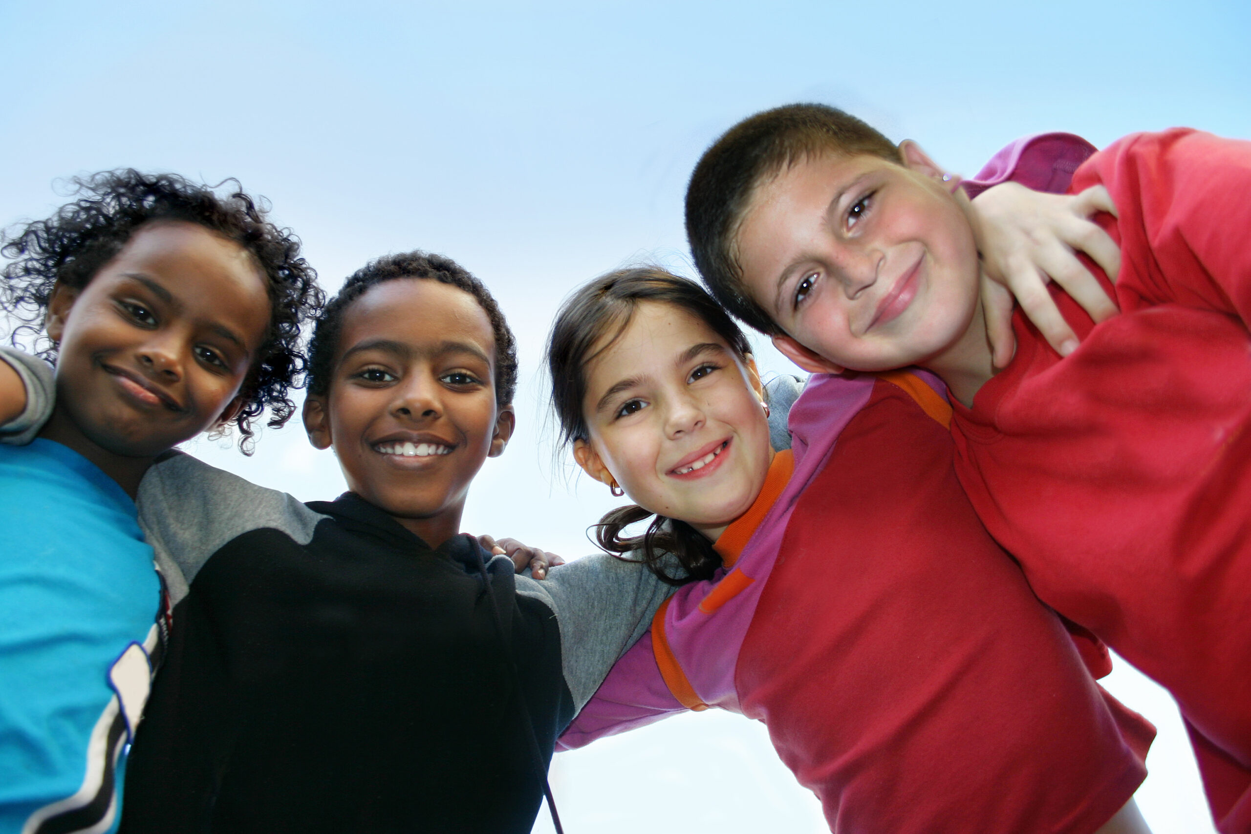 Four children of diverse ethnicities look at the camera with arms around each other