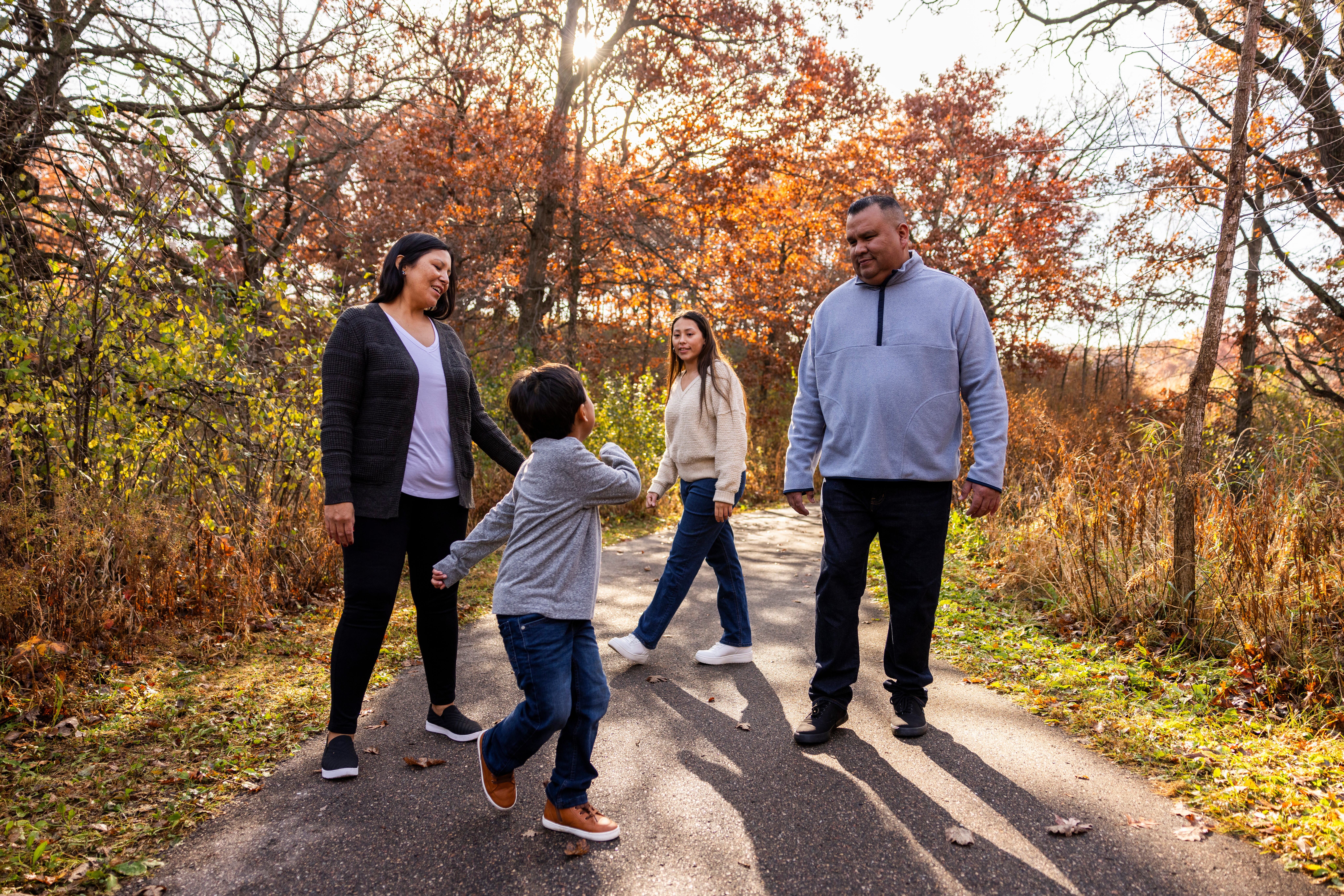 Indigenous mother, father, son and daughter walk on a trail next to trees in autumn