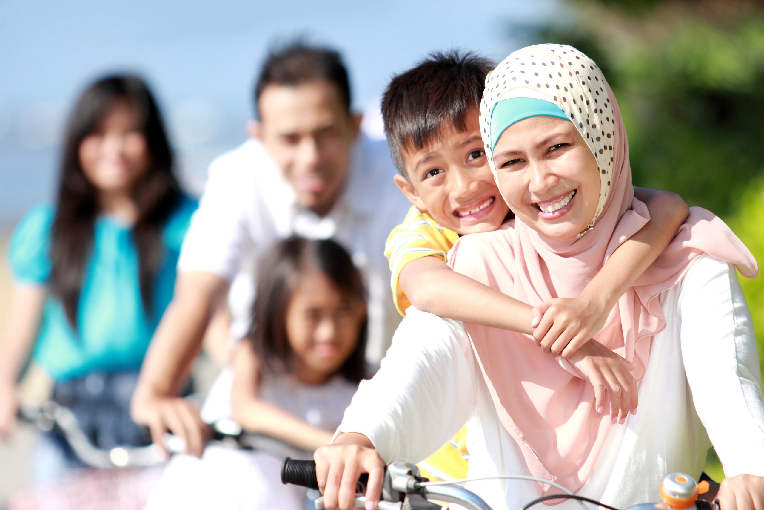 Newcomer family on bikes with focus on mother in hijab and smiling boy on her back