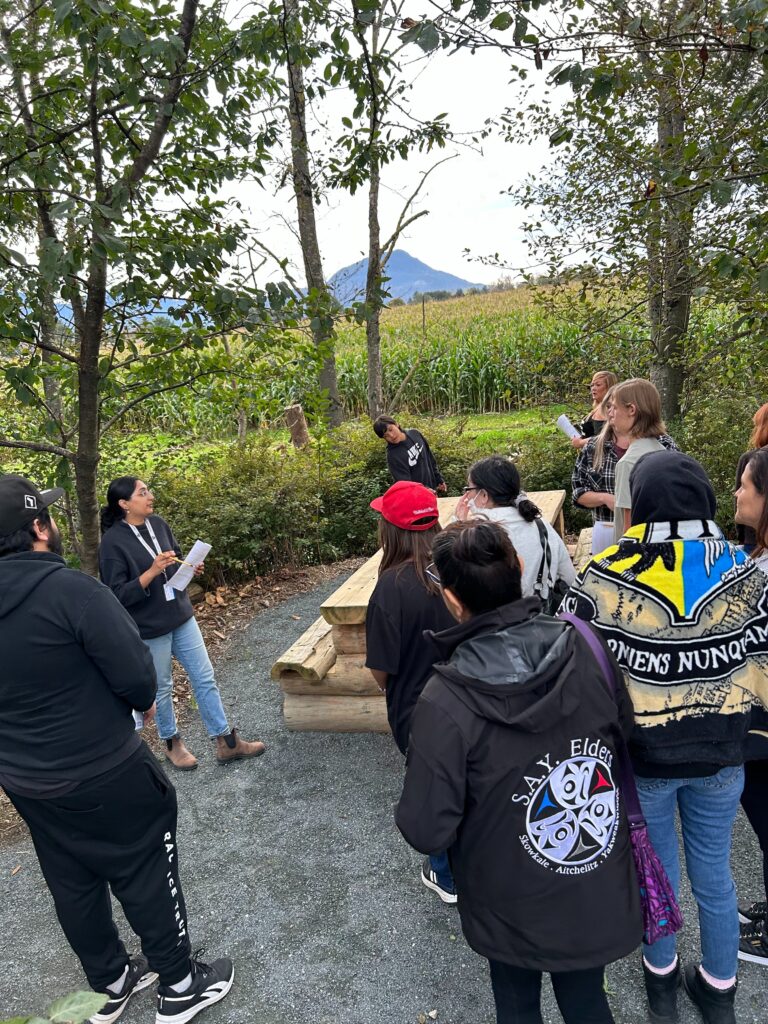 A group stands around listening to stories of Sq’ewqéyl I:mex Xalh (Skowkale Walking Path)