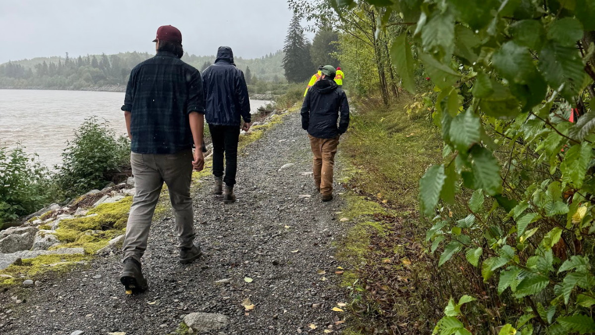 The backs of people walking in the rain on gravel on the Kitselas Cultural and Wellness Trail