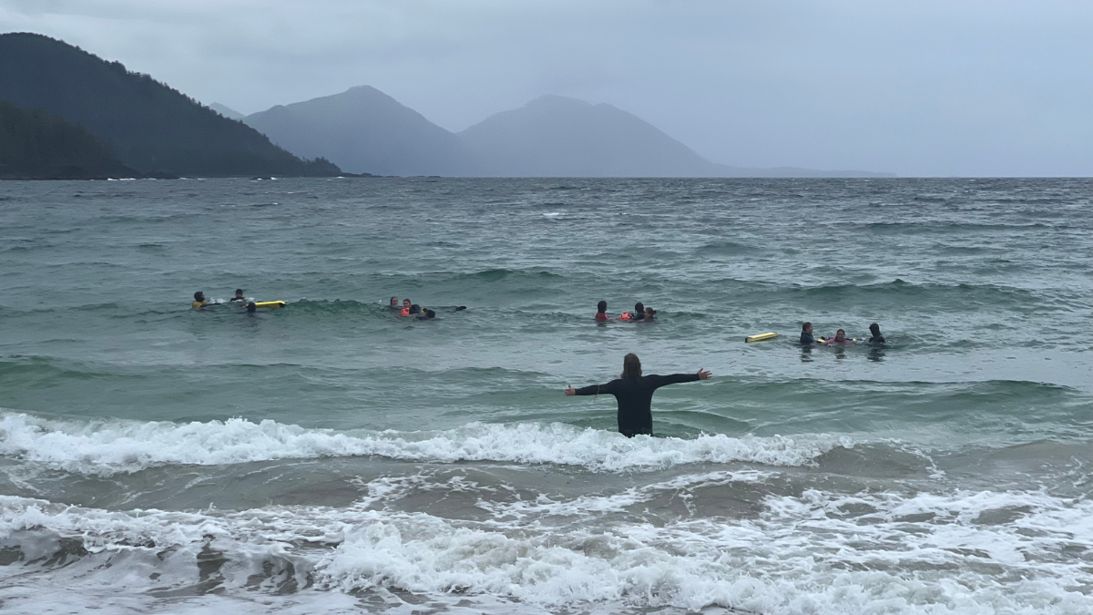 People in the water in Grant Bay doing a missing person training; one person stands with their arms out