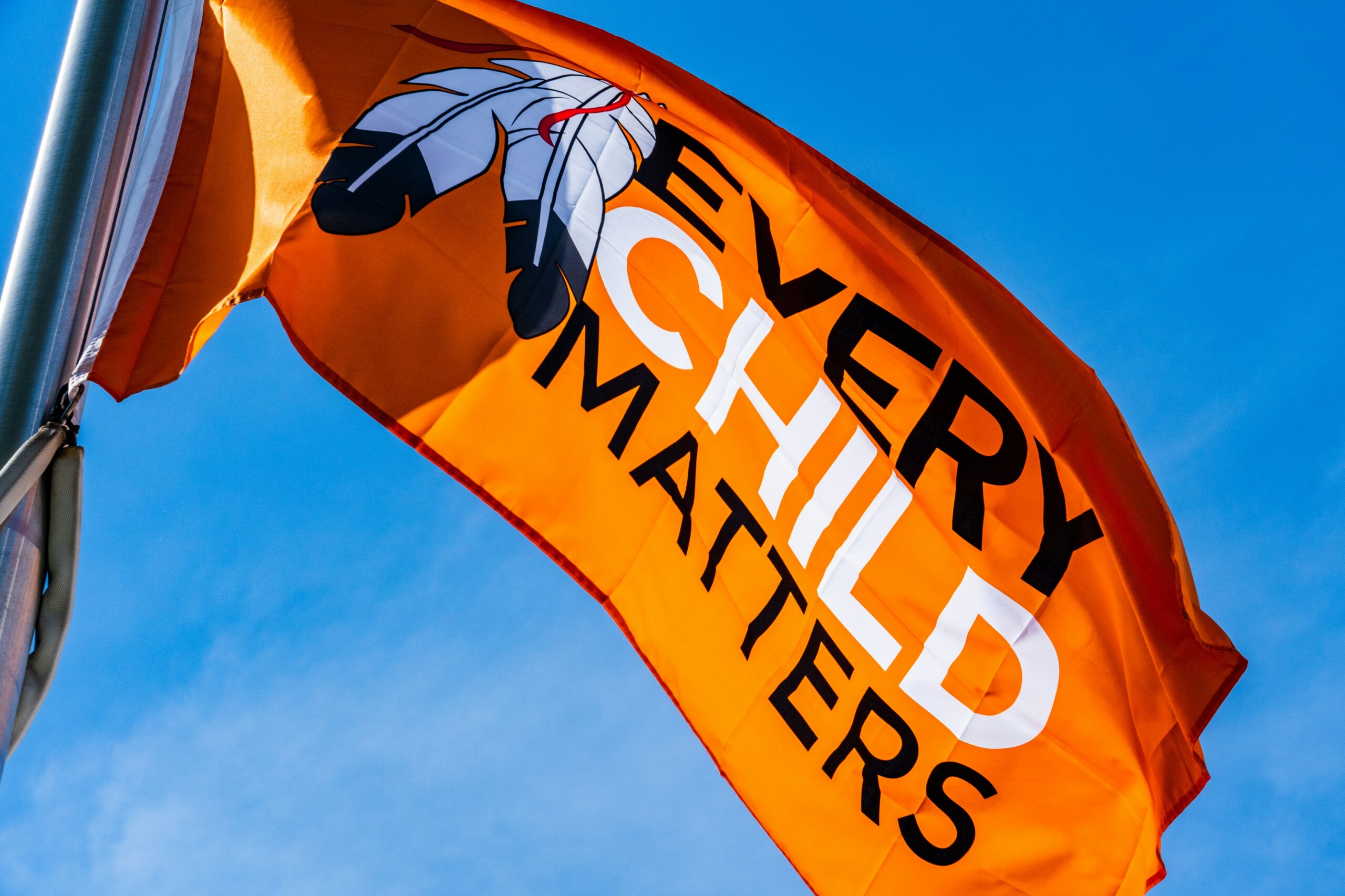 Orange flag that says Every Child Matters against a blue sky