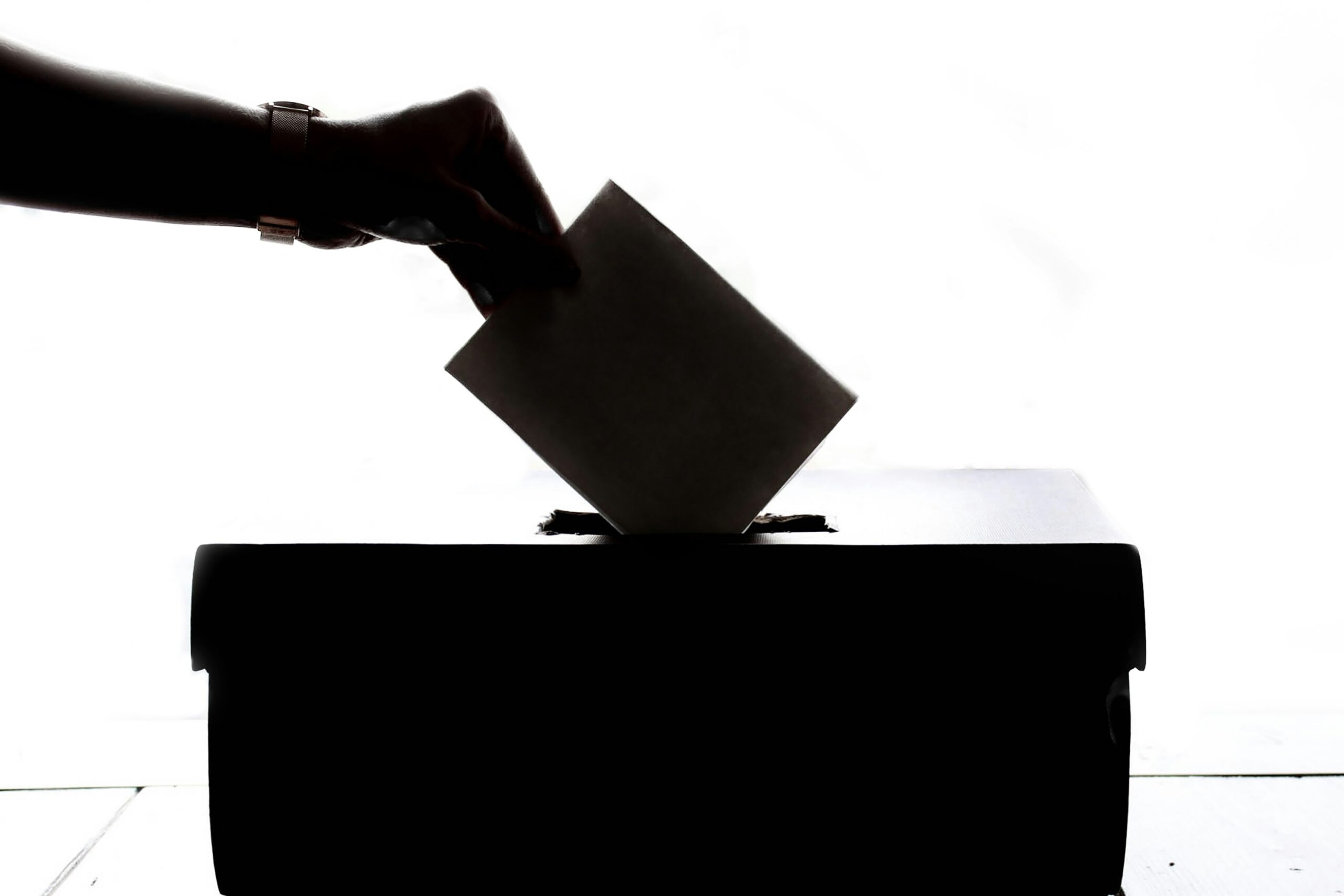 Silhouette of a person's hand holding a ballot and inserting it into the ballot box during election season.